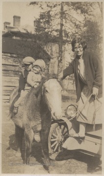 An unidentified woman on the right balances on the side of an automobile to hold onto the pony that carries the children. The persons pictured are relatives of J. D. Morris. 