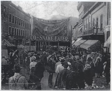 A group of men gather outside a tent where a man supposedly eats live snakes. View looking down from Temple Street toward Summers Street.