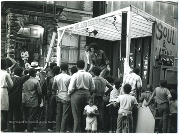 Harlem audience watching "DOPE!" by Maryat Lee.  In this scene the audience sees the characters of addict Louie (played by Michael Suner) and Porse the pusher (played by Carlo Mitton).Maryat Lee (born Mary Attaway Lee; May 26, 1923 – September 18, 1989) was an American playwright and theatre director who made important contributions to post-World War II avant-garde theatre.  She pioneered street theatre in Harlem, and later founded EcoTheater in West Virginia, a community based theater project.Early in her career, Lee wrote and produced plays in New York City, including the street play “DOPE!”  While in New York she also formed the Soul and Latin Theater (SALT), and wrote plays centered around the lives of the actors in the group.In 1970 Lee moved to West Virginia and formed the community theater group EcoTheater in 1975.  Beginning with local teenagers from the Governor’s Summer Youth Program, the rural theater group grew, and produced plays based on oral histories collected from the local community.  Each performance of an EcoTheater play involved audience participation and discussion.  With the assistance of the Humanities Foundation of West Virginia, guest scholars became a part of EcoTheater.