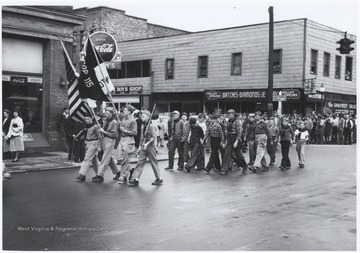 Four boys in their Boy Scout uniforms lead their troop down the street. Subjects unidentified. 