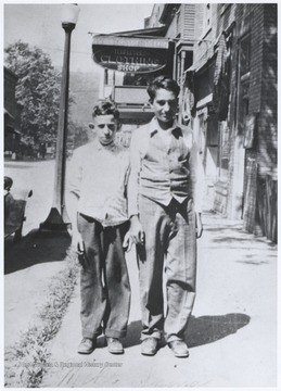 A scowling Spina, left, and his friend Coste, right, stand outside of a clothing shop. 