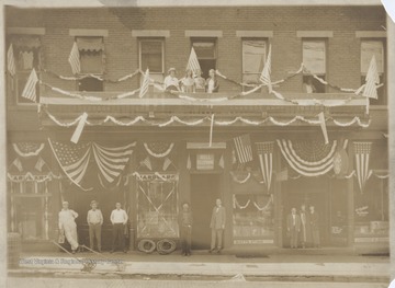 From left to right is the Hardware Store, Bell Telephone Business Office, Watt's Studio, and Sutherland Jewelry on 3rd Avenue. The store owners and clerks pose outside of their respective places. Subjects unidentified.