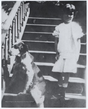 Child of Robert Murrell stands beside the Murrell dog, "Sport", on the house steps. The home is located on the corner of 5th Avenue and Summers Street. 