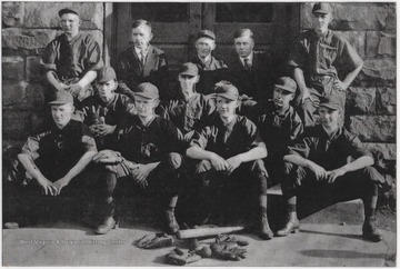 The baseball coach and players pose outside of the building for a team portrait. Subjects unidentified.