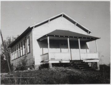 View of the schoolhouse--a white building with a small porch and plenty of windows. 