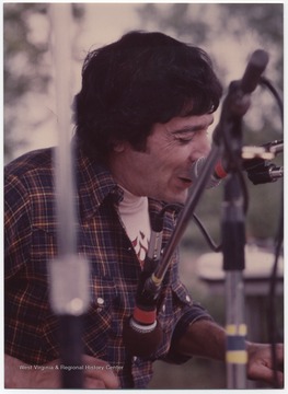 Freeman is pictured behind a set of microphones while plucking his guitar. This photograph is from a collection taken at Appalachian Folk Music Festivals, including the Ivydale and John Henry festivals. 
