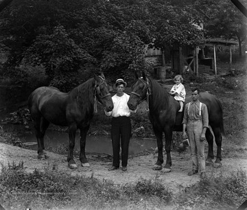 Two men and a little girl pose for a portrait with horses.