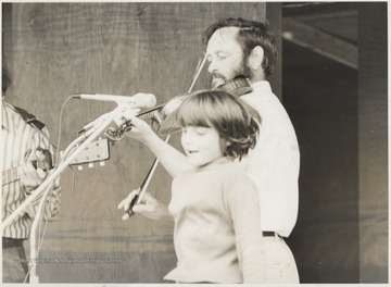Franklin George plays the fiddle with other musicians as a child dances.  This photograph comes from a series of photos from Appalachian Folk Music Festivals, including the Ivydale and John Henry festivals. 