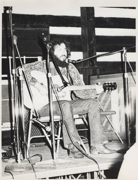 Steve Beleuw plays guitar and sings while seated behind a microphone. This photograph comes from a series of photos from Appalachian Folk Music Festivals, including the Ivydale and John Henry festivals. 