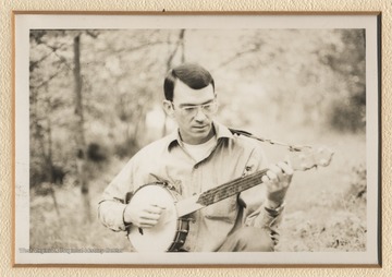 Winters plays a banjo in a wooded area at a festival. This photograph comes from a series of photographs from Appalachian Folk Music Festivals, including the Ivydale and John Henry festivals. 