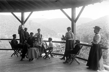 A group of unidentified individuals are pictured on a porch with a scenic view. 