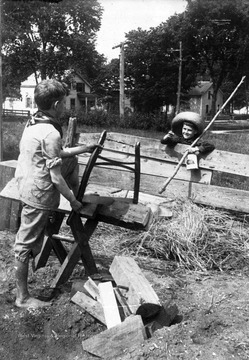 "One boy chopping wood, another with a fishing pole [is] beckoning him."  Subjects unidentified. 