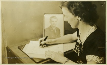 Portrait of Alice E. Parker, wife of Joseph W. Parker, of Fairmont, W. Va., soldier in World War II, as she writes a letter.  A portrait of her husband is in the background.