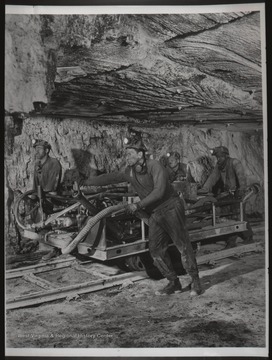 Coal miners push a large machine on tracks in an unknown mine likely in West Virginia.