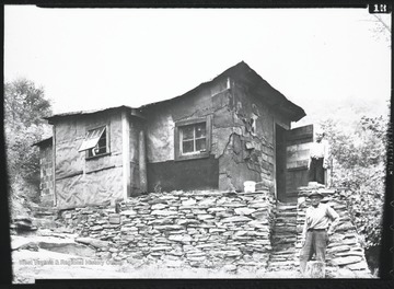 Two men stand outside of a mine camp house in an unknown location.