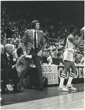 West, wearing a patterned blazer, with Jack McCloskey, left, look out onto the court as the game progresses. After fourteen years of playing for the team, West rejoined the Lakers as coach for three seasons between 1976 and 1982. He led the team to the playoffs each season. 
