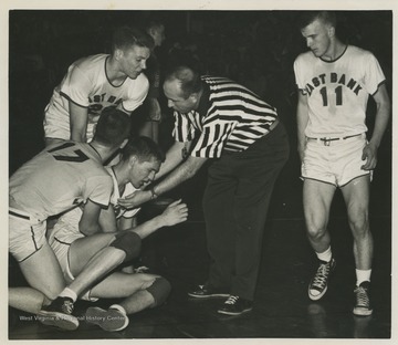 A referee and teammates come to West's aid during a high school basketball game.West was the East Bank High School's starting small forward. He was named All-State from 1953–56, then All-American in 1956 when he was West Virginia Player of the Year, becoming the state's first high-school player to score more than 900 points in a season.The 1956 team secured the first ever state championship title for East Bank High School's basketball team. 