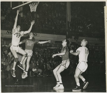East Bank High School's Gary Stover, No. 17, drives in for a layup while Mullens High School's Gene Miller tries to halt the play. Also pictured is Mullens player Ronnie Cook and East Bank player Jack Landers, No. 11.Jerry West was also a player in this game and led the team to victory. The 1956 team secured the first ever state championship title for East Bank High School's basketball team.West was East Bank High School's starting small forward. He was named All-State from 1953–56, then All-American in 1956 when he was West Virginia Player of the Year, becoming the state's first high-school player to score more than 900 points in a season.