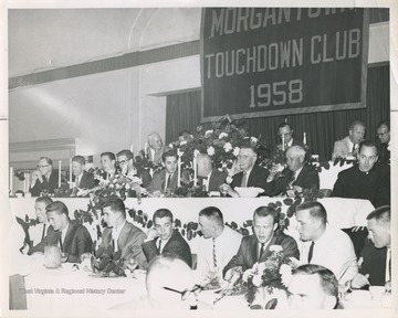 A group of men are gathered at a spring banquet held at Hotel Morgan after the West Virginia University basketball team was ranked No. 1 in the United States.In the front row, from left to right, is unidentified, Jerry West, Bobby Joe Smith, Ronnie Retton, Bucky Bolyard, Butch Gude, Jim Warren, and possibly Willie Akers.In the second row, from left to right, is athletic director Red Brown, basketball referee Red Mahalic, Jody Gardner, Loyd Sherer, Don Vincent, Whitie Guyme, team physician Dr. Sam Morris, Golf-pro Reggie Spencer, and Father Scott.In the third row, from left to right, is University of Pittsburgh basketball coach Doc Cartson, WVU head coach Fred Schaus, unidentified, the team's general manager Mr. Gwair, and unidentified. 