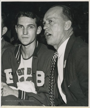 Williams, right, seems to be telling his star, Jerry West, left, not to worry after West fouled out of the game with 5:27 minutes left to play.West lead East Bank High School to secure its first ever state championship title as the team's starting small forward. He was named All-State from 1953–56, then All-American in 1956 when he was West Virginia Player of the Year, becoming the state's first high-school player to score more than 900 points in a season.