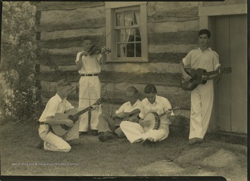 The unidentified boys play their string instruments outside of a log building in an unidentified location. 