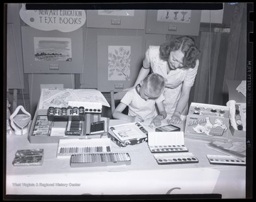 A woman looks over a young boy's shoulder as he colors with a crayon from the display. Subjects unidentified. 