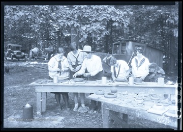 A man shows the girls how to effectively decorate a clay pot. Subjects unidentified. 