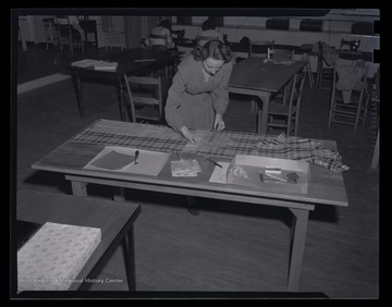 An unidentified woman is sewing fabric at a table. 