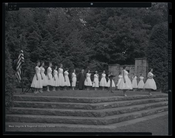A group stands on an outdoor stage in preparation for the coronation ceremony. 