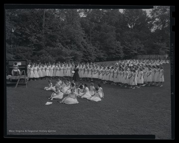 A group of girls are gathered to sing on a lawn. Subjects unidentified. 