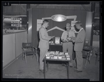 A group of men look at sample bottles and pamphlets at the dairy show.