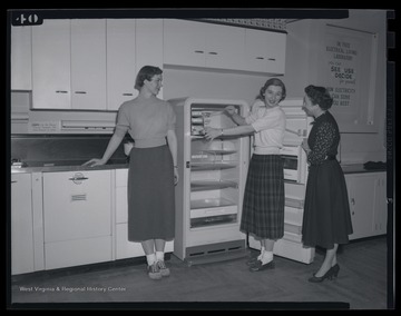 Three unidentified girls work with a refrigerator's ice box. 