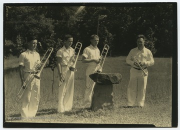 Three trombone players and one trumpeter pose beside what appears to be a grave marker. 