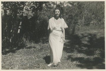 Portrait of Pearl S. Buck in a white dress standing under a tree, location unknown.
