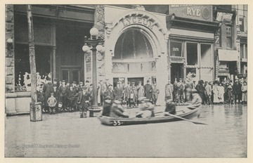 Photo postcard showing the Lyceum Theater in Wheeling during the 1913 flood.  A group of people paddles a boat down the street. Postcard is part of a souvenir book of 1913 flood images.