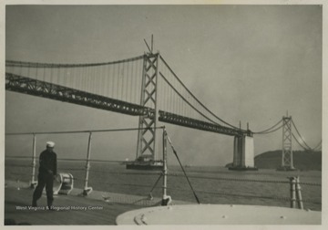 A sailor walks along the deck while the ship passes the bridge. 