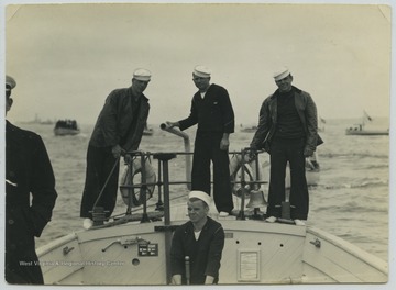 A crew consisting of a cox, and engineer and two extra men are pictured on the stem of the boat, which was used to take enlisted men ashore. The boat carries about 125 men and is 50 feet long. 