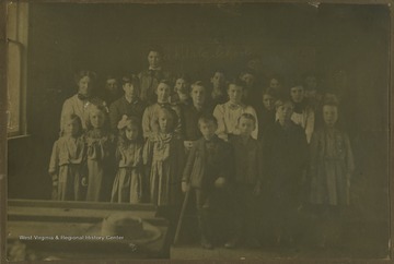 A group of school children and their teacher are pictured inside of a school building. In the background, "Oakdale School" is written on the chalkboard. Subjects unidentified. The photograph comes from a photo album belonging to Mrs. Earl R. Zinn.