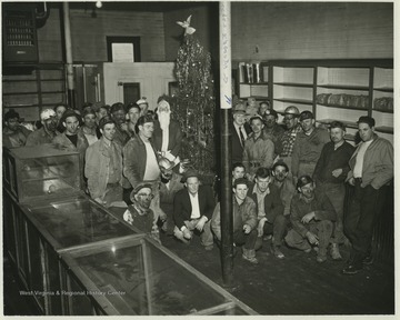 Miners of the Zephyr Mine are gathered around a Christmas tree. The man standing on the right side of the tree with a hat and suit is Rush Meadows, a mining engineer and operator from Charleston, W. Va.