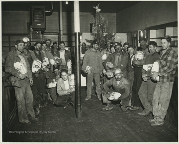 Miners of the Zephyr mine hold on to their wrapped hams in front of a Christmas tree. Subjects unidentified. 