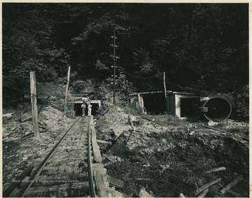 Two unidentified men stand on the railway that leads into the mine entrance. 