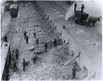 Men carry coal from a railroad car and shovel coal into furnaces. 
