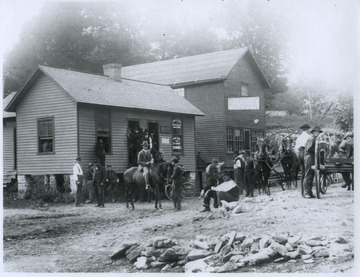 Men and horses are gathered in front of the buildings. James L. Long, Attorney at Law and Notary Public, advertises fire, life, and accident insurance.  The Photograph Gallery advertises frames and art novelties for low prices.