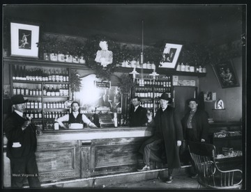 Men stand beside the bar, holding drinks.