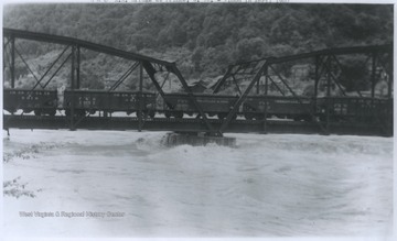 A Chesapeake and Ohio Railroad train moves across the bridge while flood water rushes beneath. 