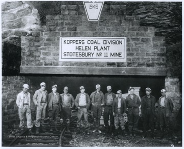 Eleven miners are pictured outside of a mine entrance. 