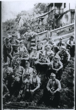 A group of miners sit on a hill with their mining equipment. One of the miners holds a small boy on his lap.