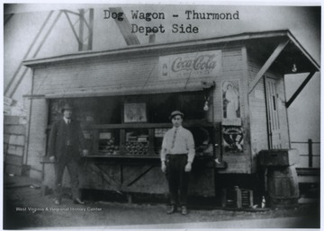 P. H. Kelly and a colleague stand outside of a dog wagon--a small restaurant often specializing in short orders that occupies a converted vehicle or that is built to suggest such a vehicle.