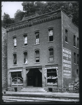 On the left, a man stands at the window of New River Banking & Trust Co. On the right is Mankin Drug Co. 