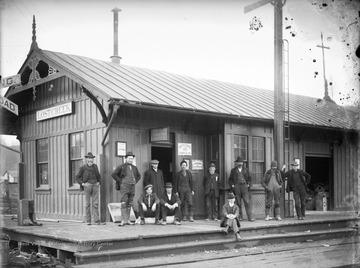 A group of men are pictured loitering outside of the Lost Creek Station Western Union Telegraph Office. In the background is an advertisement for United States Express Company Money Orders. 